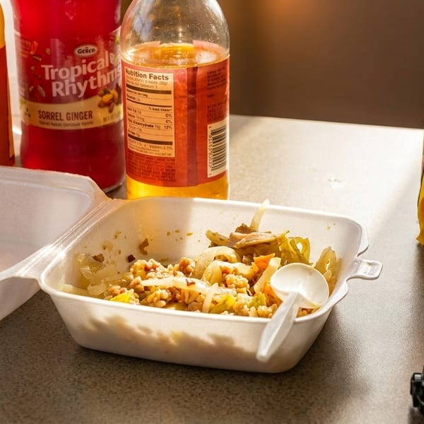 Half-eaten takeout meal in a styrofoam container with bottles of drinks and a toy car.